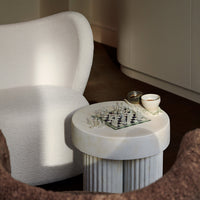 White plush chair, marble-striped side table with chessboard, neutral tones, soft textures, minimalist design elements.