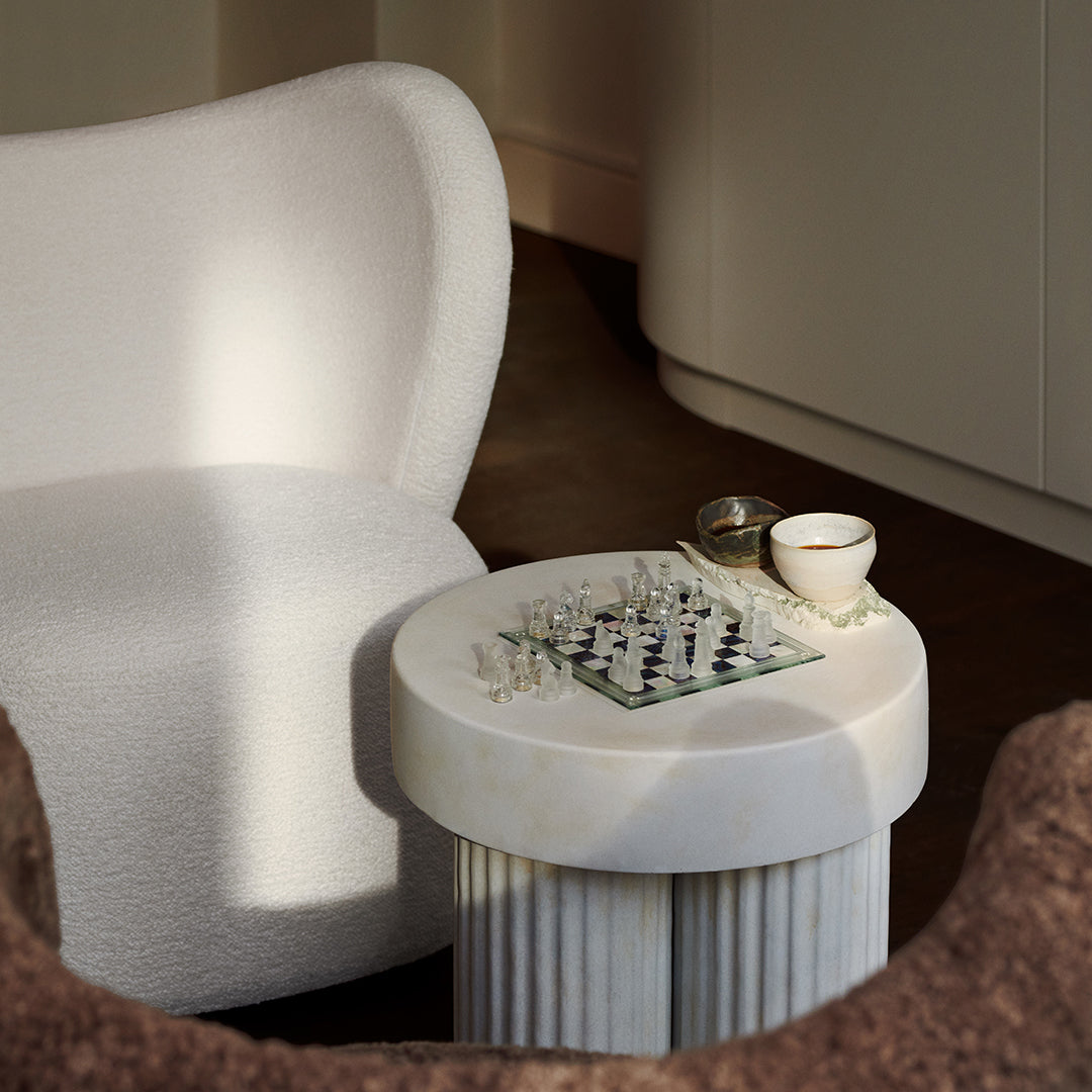 White plush chair, marble-striped side table with chessboard, neutral tones, soft textures, minimalist design elements.