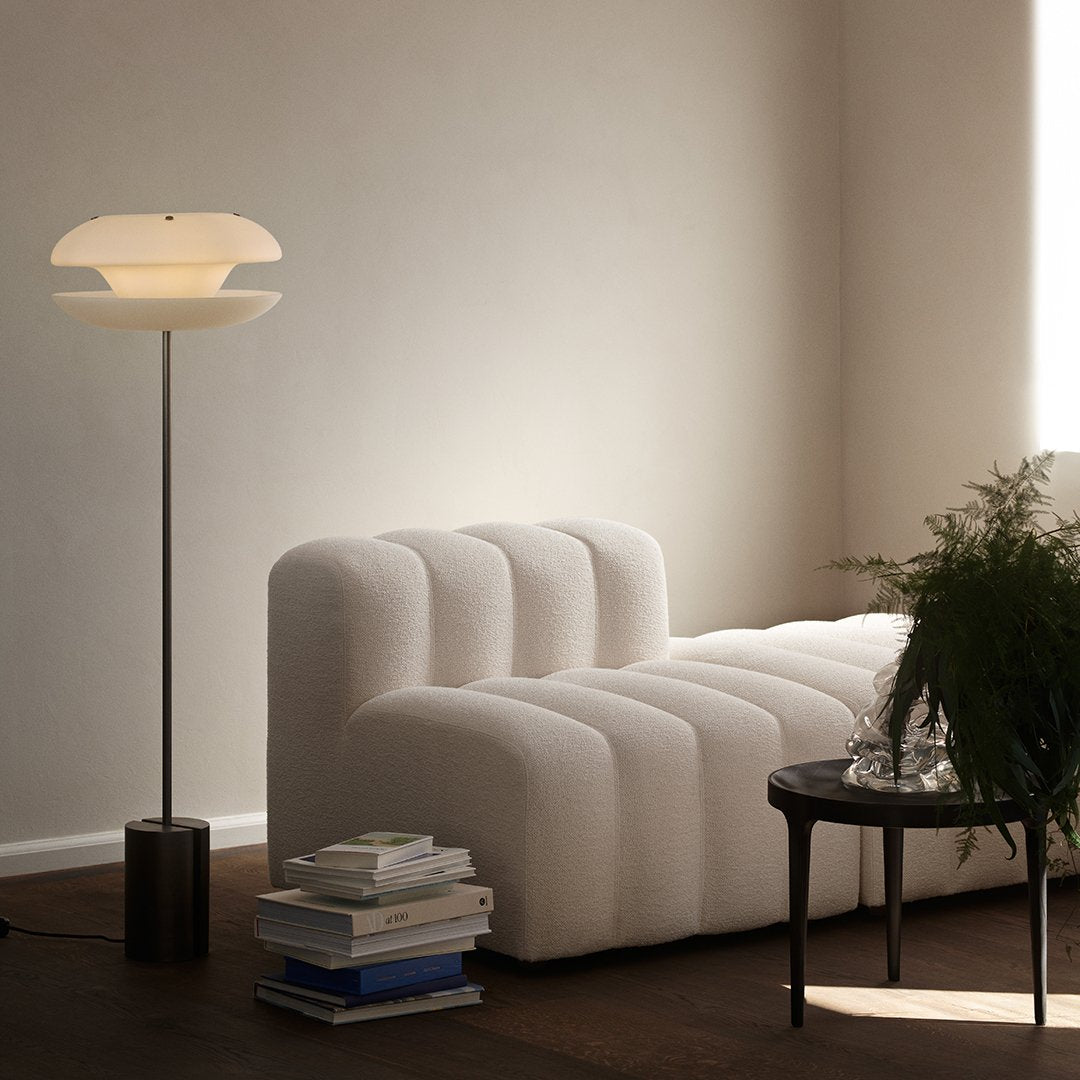 White textured sofa with soft curves, accompanied by a sleek black table and a warm-toned lamp, creating a modern aesthetic.