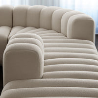 Beige curved sofa with textured, vertical lines and plush, rounded armrests in a modern design.