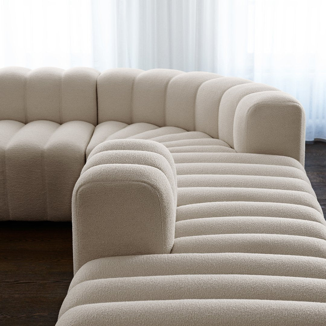 Soft beige curved sofa with textured, ribbed fabric pattern and rounded edges, perfect for modern interiors.