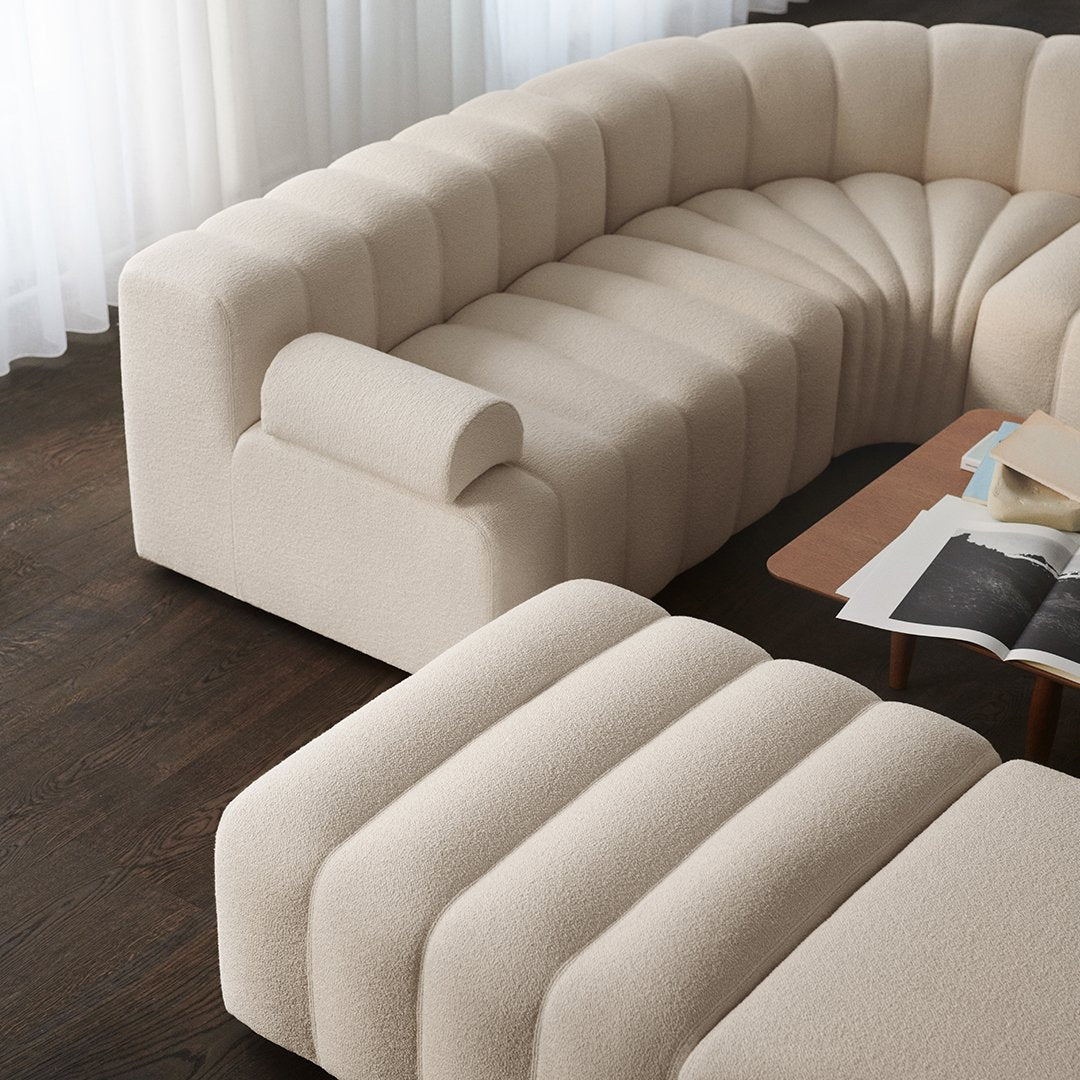 Beige curved sofa with vertical ribbed texture, paired with a wooden coffee table and soft, neutral decor.