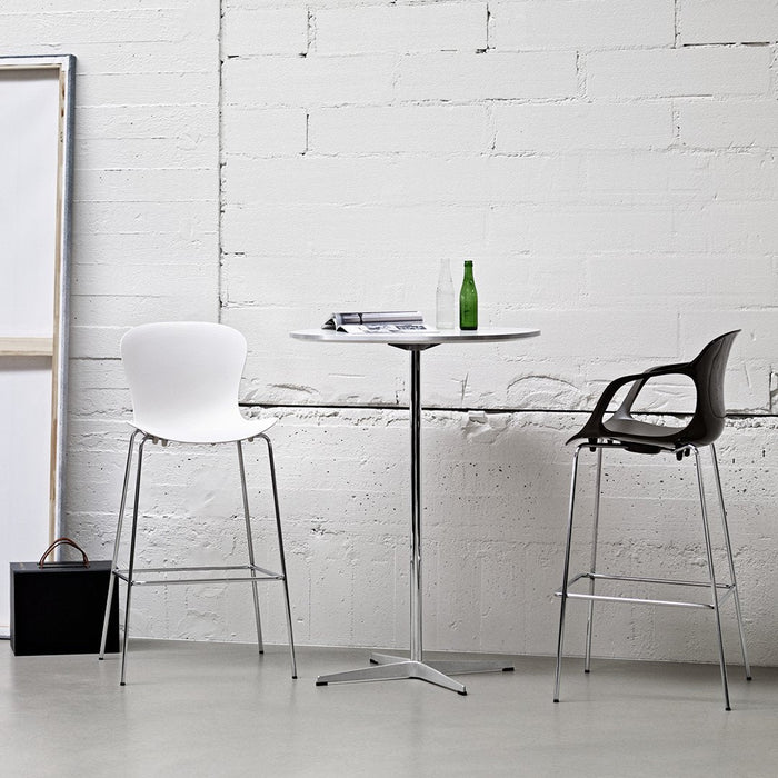 Modern white and black bar stools around a sleek round table, set against a minimalist white brick wall.
