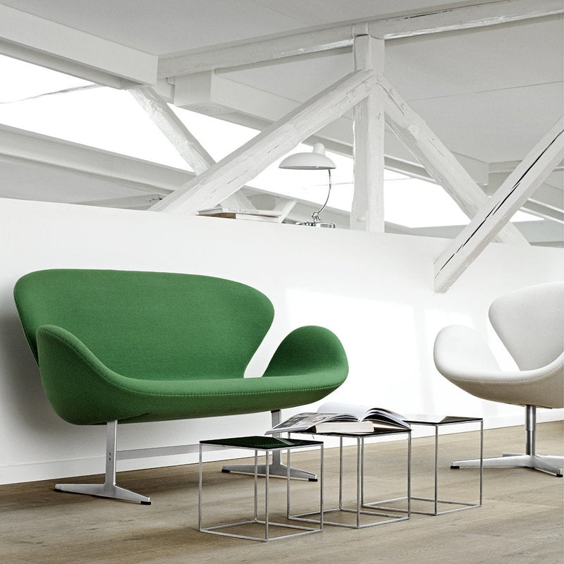 Green fabric chair with smooth curves, contrasted against a minimalist white chair and wooden floor. Modern design accents.