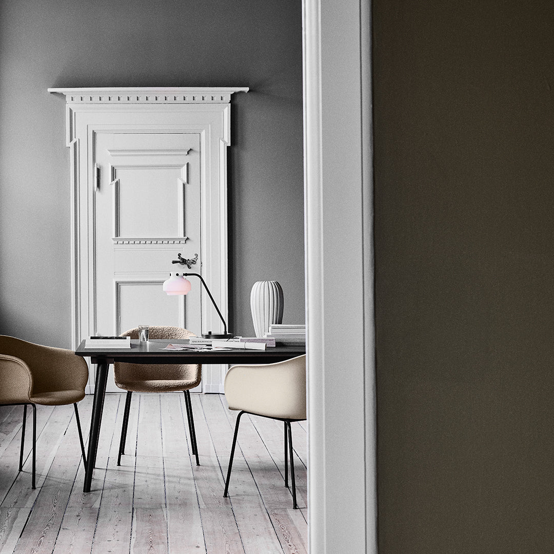 Modern neutral decor with a light gray wall, white trim, beige chairs, and soft pink lamp on a dark wood table.