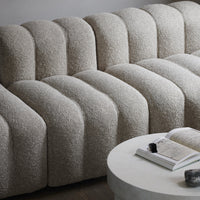 Beige sculptural sofa with soft, curved lines and a textured, plush upholstery pattern. Modern, minimalist design.
