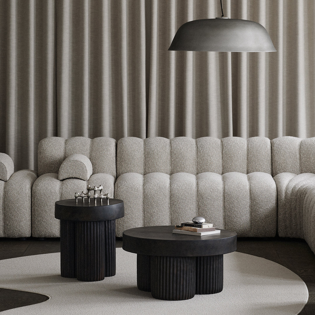 Grey textured sofa with black round tables and a curved light fixture, set on a soft circular rug. Elegant modern design.