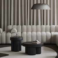 Grey textured sofa with black round tables and a curved light fixture, set on a soft circular rug. Elegant modern design.