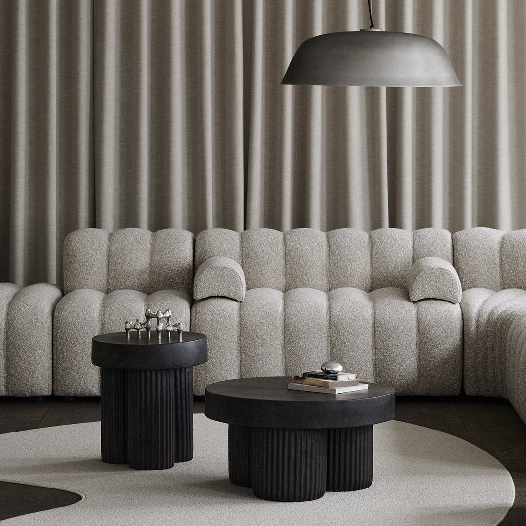 Grey tufted sofa, black sculptural coffee tables, neutral carpet, and patterned curtains create a modern minimalist aesthetic.