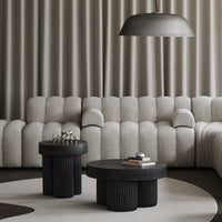 Grey tufted sofa, black sculptural coffee tables, neutral carpet, and patterned curtains create a modern minimalist aesthetic.