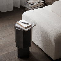 Stylish black geometric side table with a smooth finish, complementing a textured cream sofa and wooden flooring.