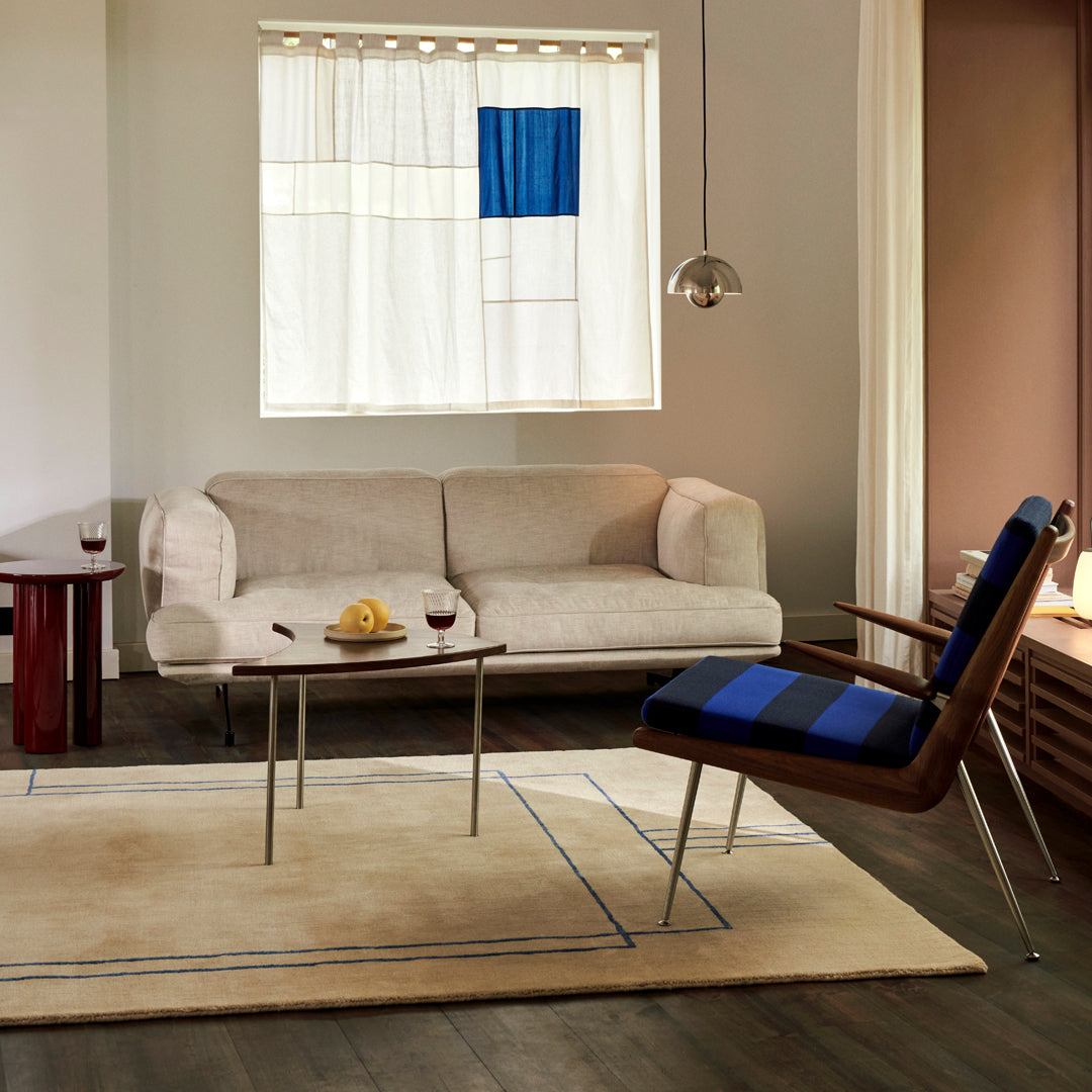 Modern living room with beige sofa, blue plaid chair, neutral area rug, and colorful window curtains.