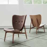 Two stylish mid-century chairs in rich brown and white leather with wooden frames, set against a modern geometric floor.