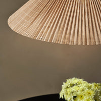 Beige pleated lampshade with a textured pattern, complementing a dark base and soft green floral arrangement.