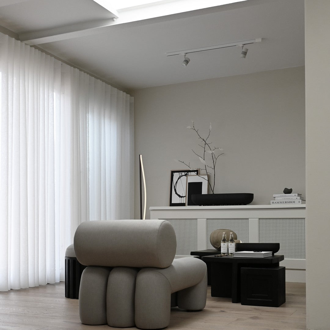 Gray sculptural seating and black accent tables against a neutral backdrop with white sheer curtains. Cozy modern decor.