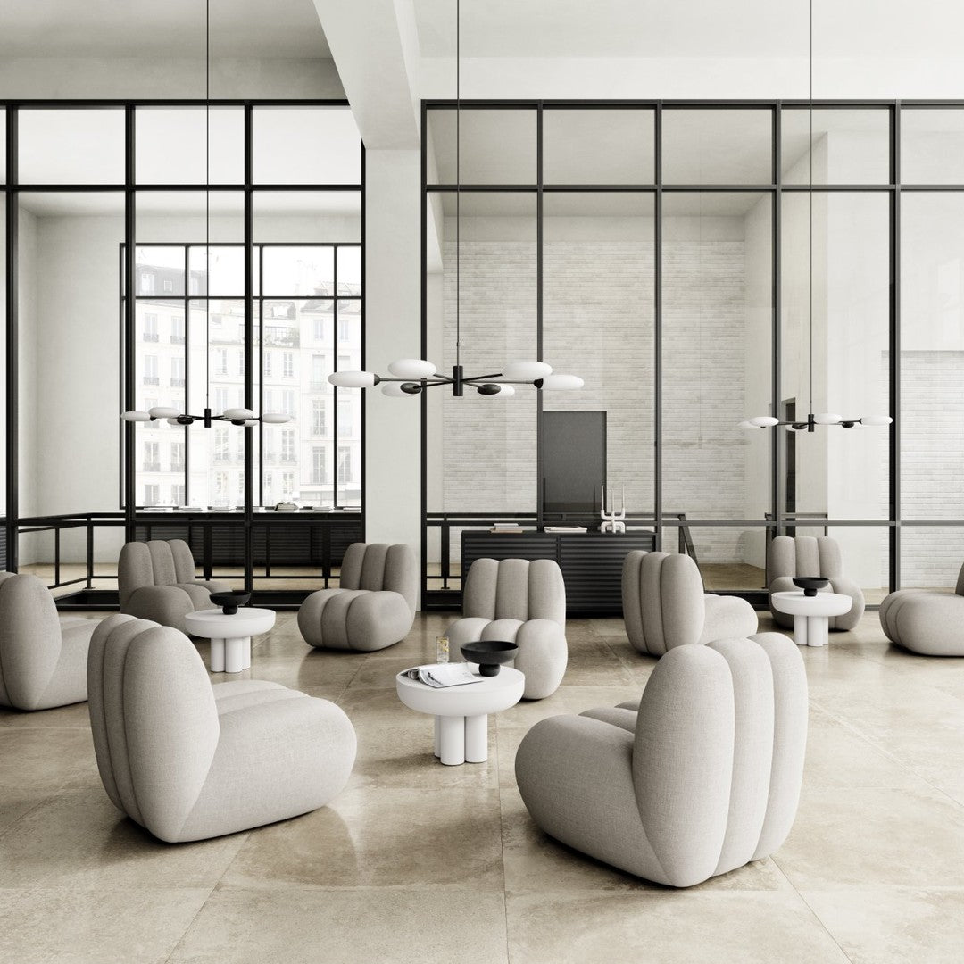 Light gray upholstered chairs and tables with soft curves in a modern, minimalist setting. Black accents enhance the design.