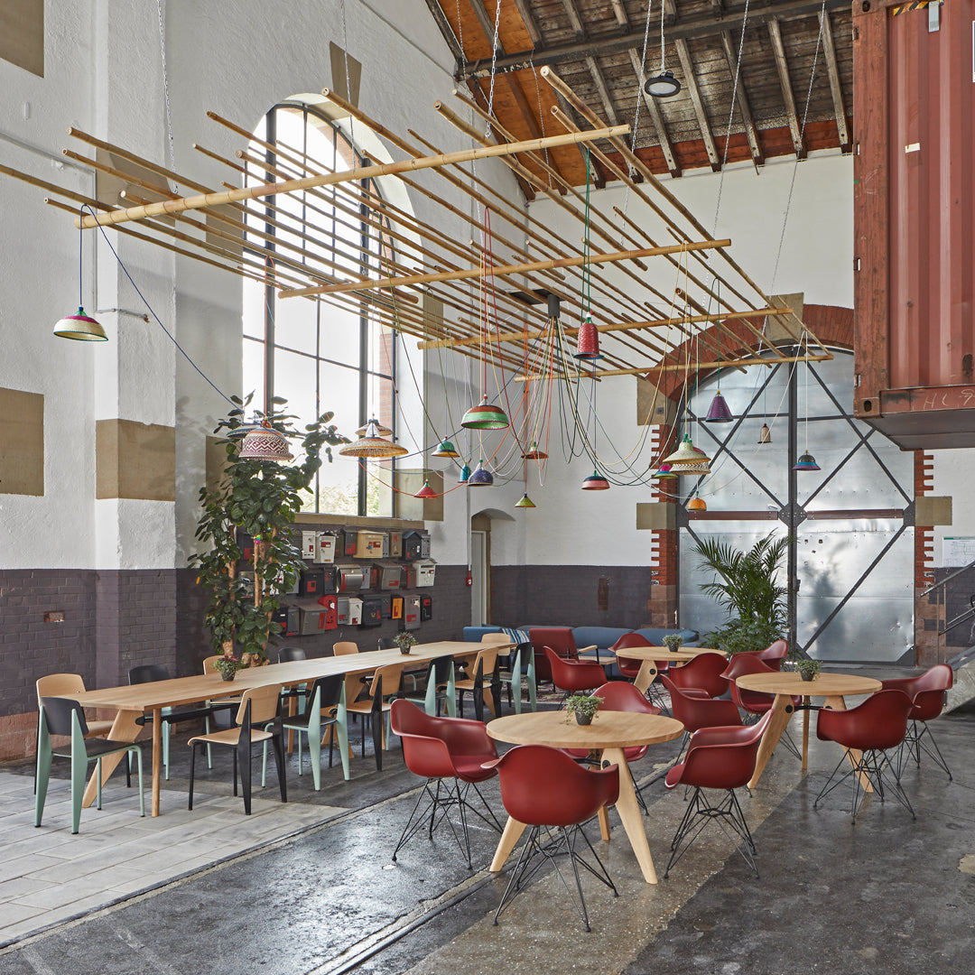 Brightly colored hanging lights contrast against rustic wooden beams in a modern, open dining space with red and green chairs.