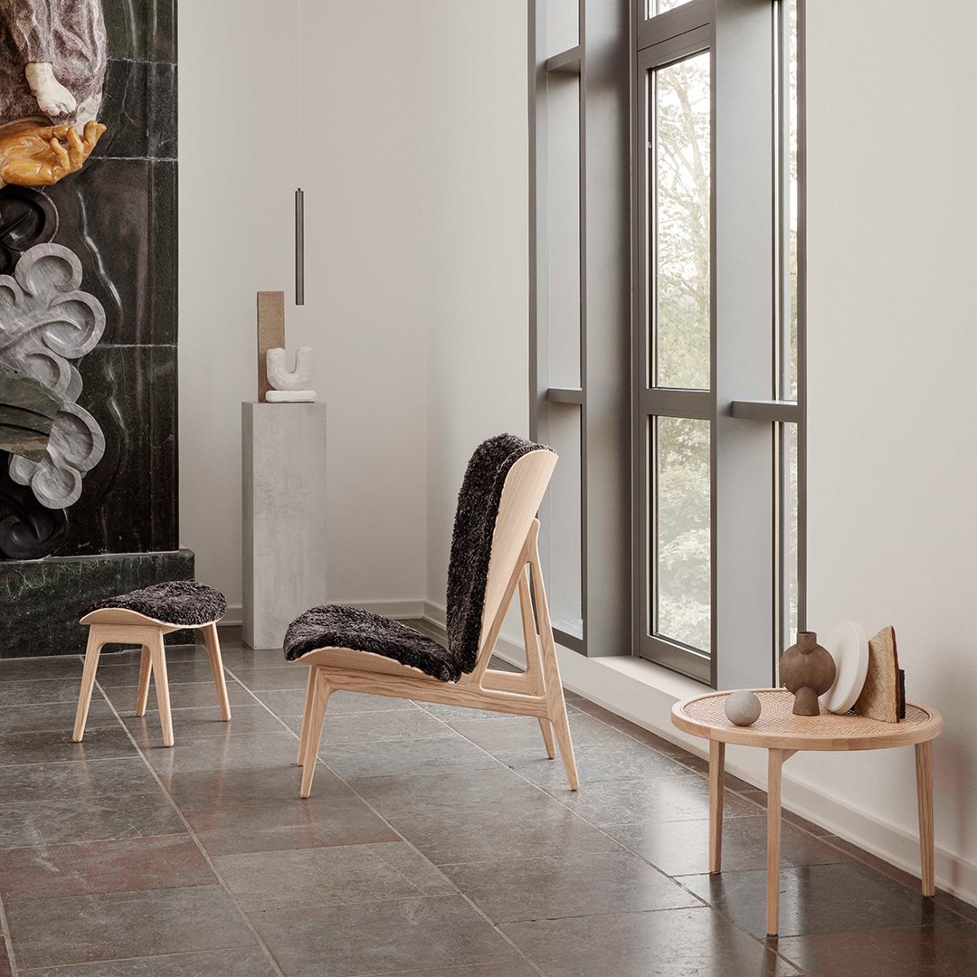 Modern wooden chair and stool with dark patterned upholstery, set against a minimalist interior with neutral tones.