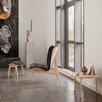 Modern wooden chair and stool with dark patterned upholstery, set against a minimalist interior with neutral tones.