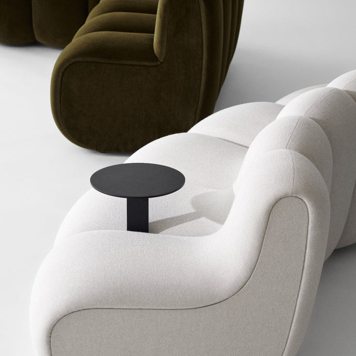 Modern sofa featuring a creamy white fabric with smooth curves and an optional black side table against deep green upholstery.