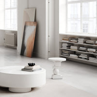 Modern living room with a white round table, warm-toned abstract art, and neutral colored books on shelves.