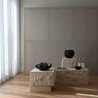 Black ceramic vases on textured stone pedestals against a neutral beige background, highlighted by soft natural light.