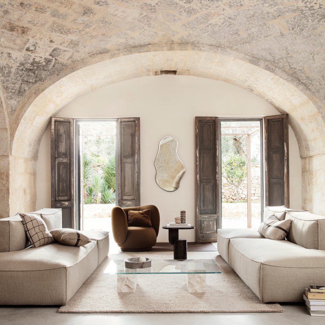 Beige sofas with geometric patterns, chocolate brown accent chair, light natural wood accents, and stone textured walls.