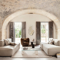 Beige sofas with geometric patterns, chocolate brown accent chair, light natural wood accents, and stone textured walls.