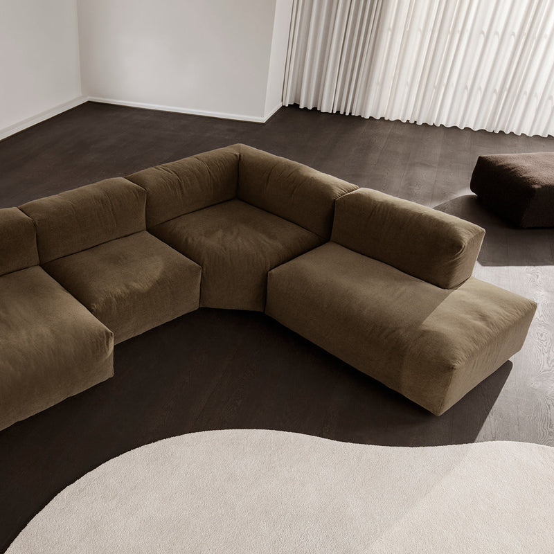Brown sectional sofa in a modern living room with a soft, curved area rug and light, neutral curtains.