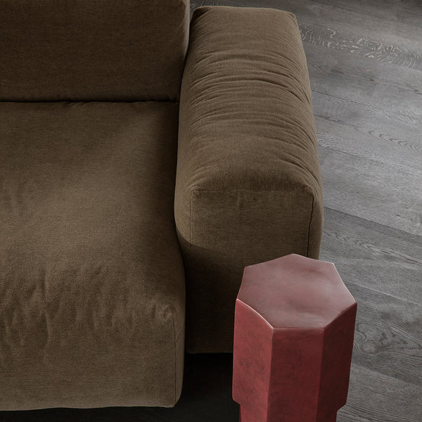 Brown velvet sofa with a plush texture and a contrasting red hexagonal side table against a dark wood floor.
