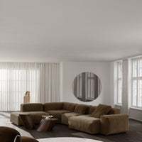 "Cozy brown sectional sofa in a minimalist white room with soft textures and geometric patterns."