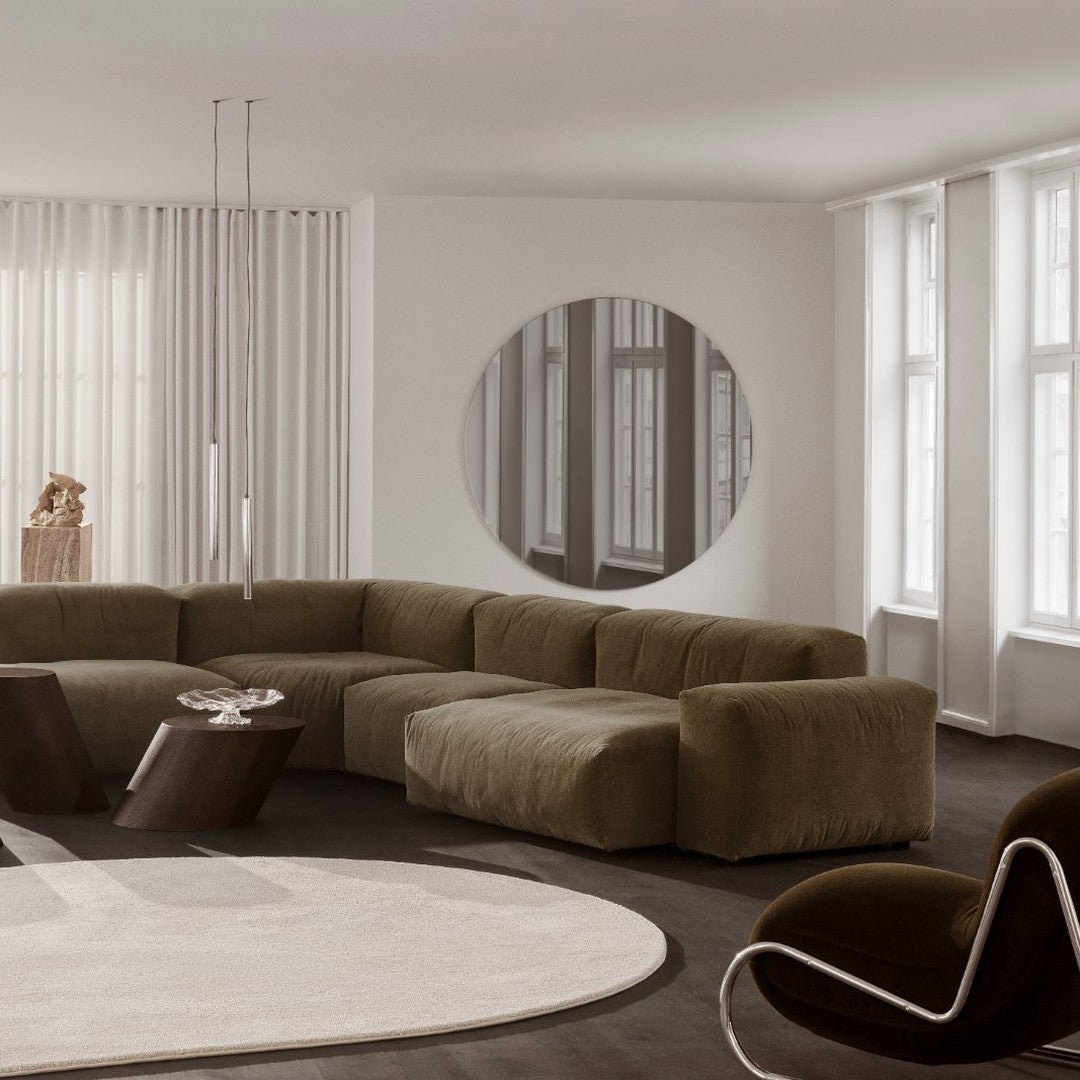 Stylish curved sofa in earthy olive green, complemented by a round mirror and contrasting dark wood accents.