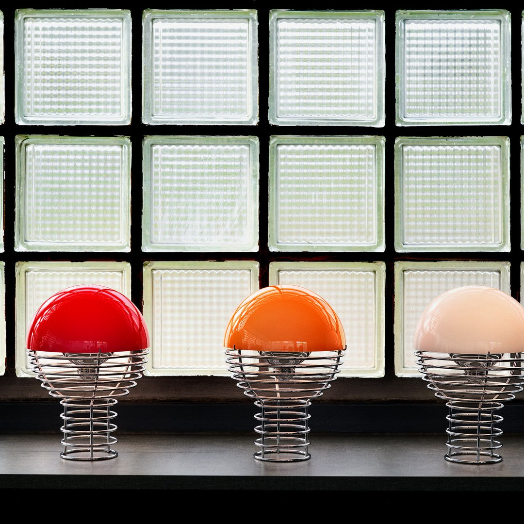 Colorful spherical lamps in red, orange, and white with sleek metal springs, set against a textured glass backdrop.