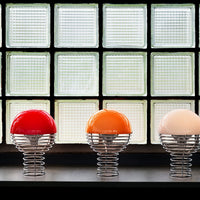 Colorful spherical lamps in red, orange, and white with sleek metal springs, set against a textured glass backdrop.