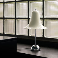 White bell-shaped lamp with a glossy finish, chrome base, and minimalist design, set against textured glass blocks.