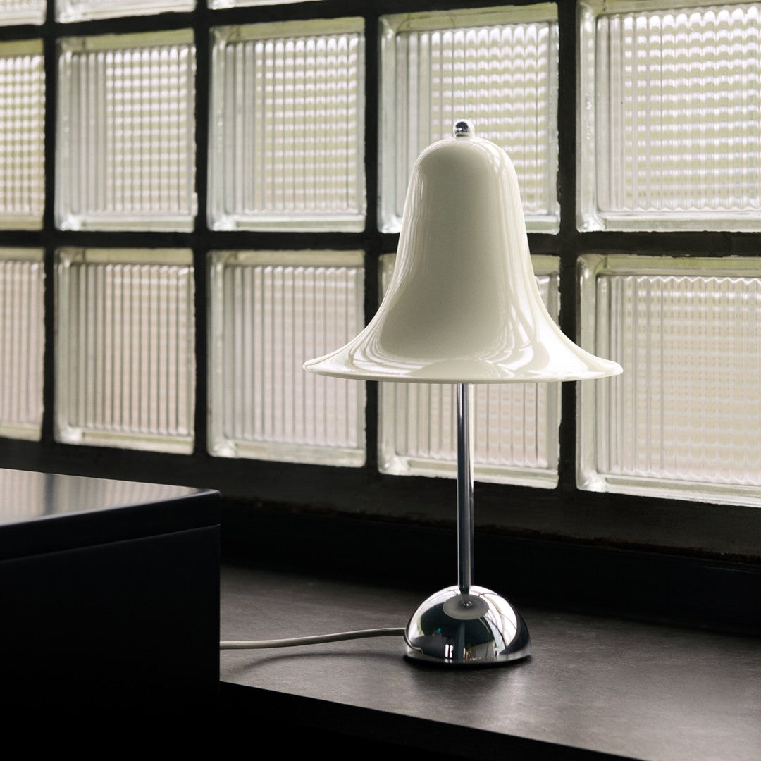 White bell-shaped lamp with a shiny chrome base, set against textured glass block background. Modern design element.