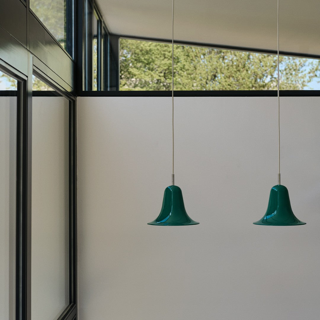 Two green bell-shaped pendant lights hanging against a minimalist interior with a white backdrop and large windows.