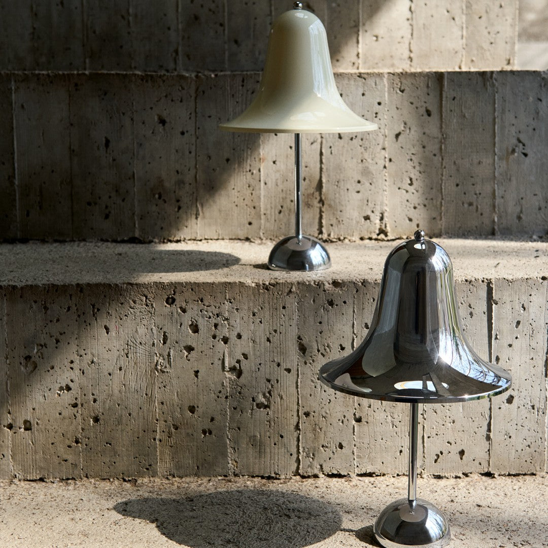 Two bell-shaped lamps in matte white and shiny chrome, contrasting against textured concrete surfaces.