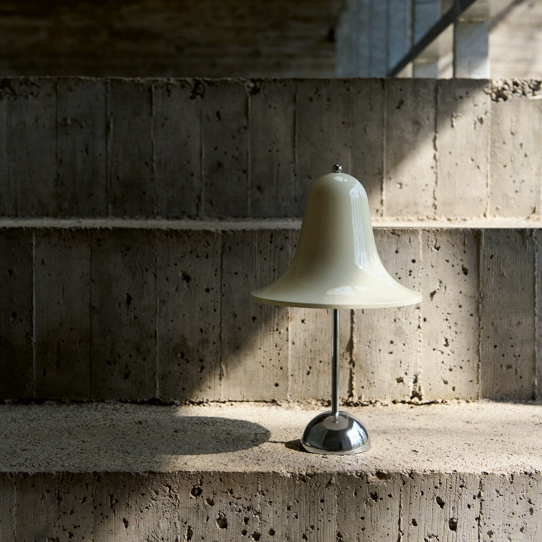 Cream-colored bell lamp with a chrome base, set against textured concrete steps, highlighting minimalistic design.