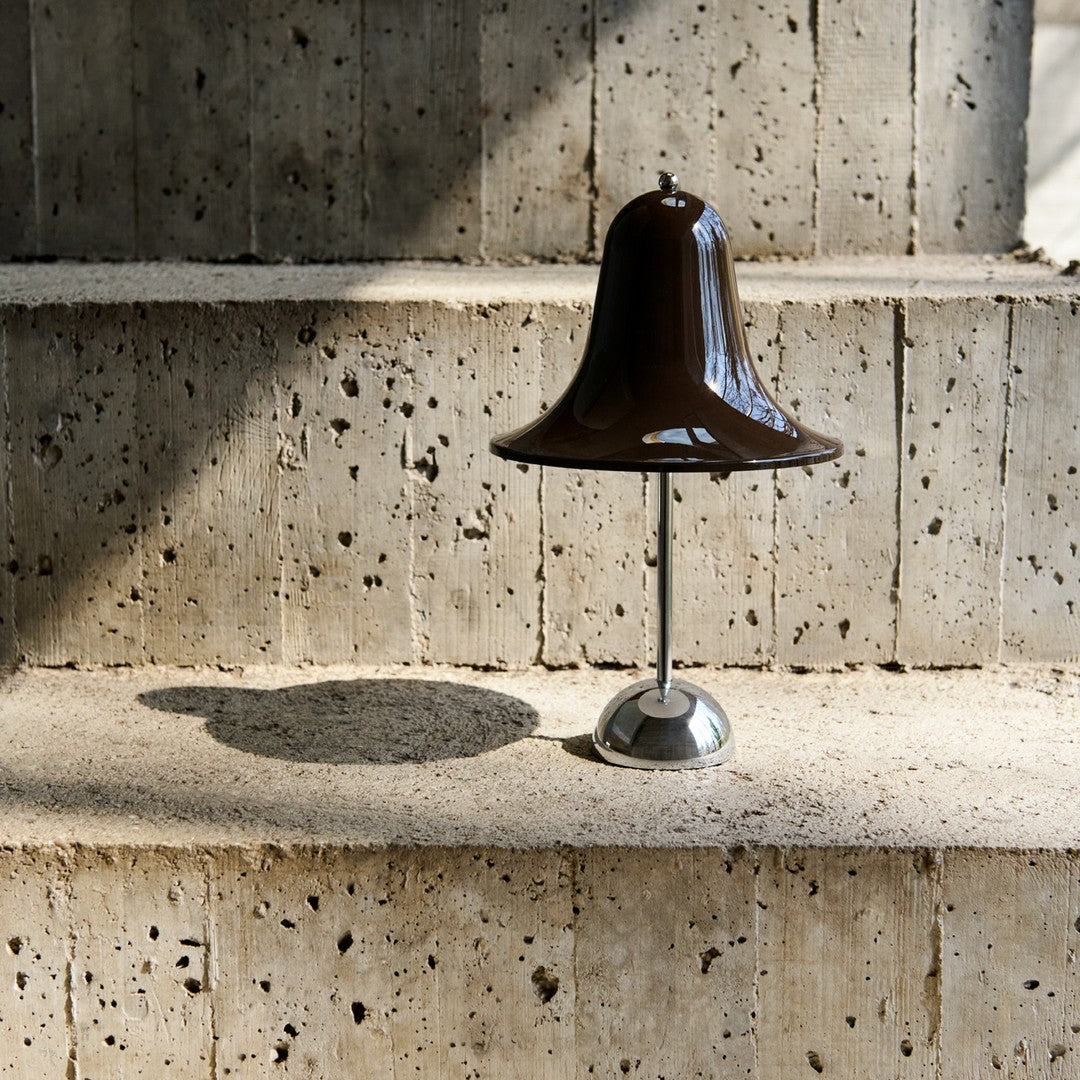 Brown bell-shaped lamp on a textured concrete surface, featuring sleek metallic accents and soft shadows.