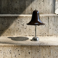 Brown bell-shaped lamp on a textured concrete surface, featuring sleek metallic accents and soft shadows.