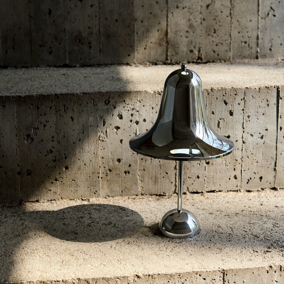 Shiny silver bell-shaped lamp on textured stone steps, casting soft shadows in warm, natural light.