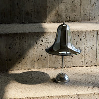Shiny silver bell-shaped lamp on textured stone steps, casting soft shadows in warm, natural light.