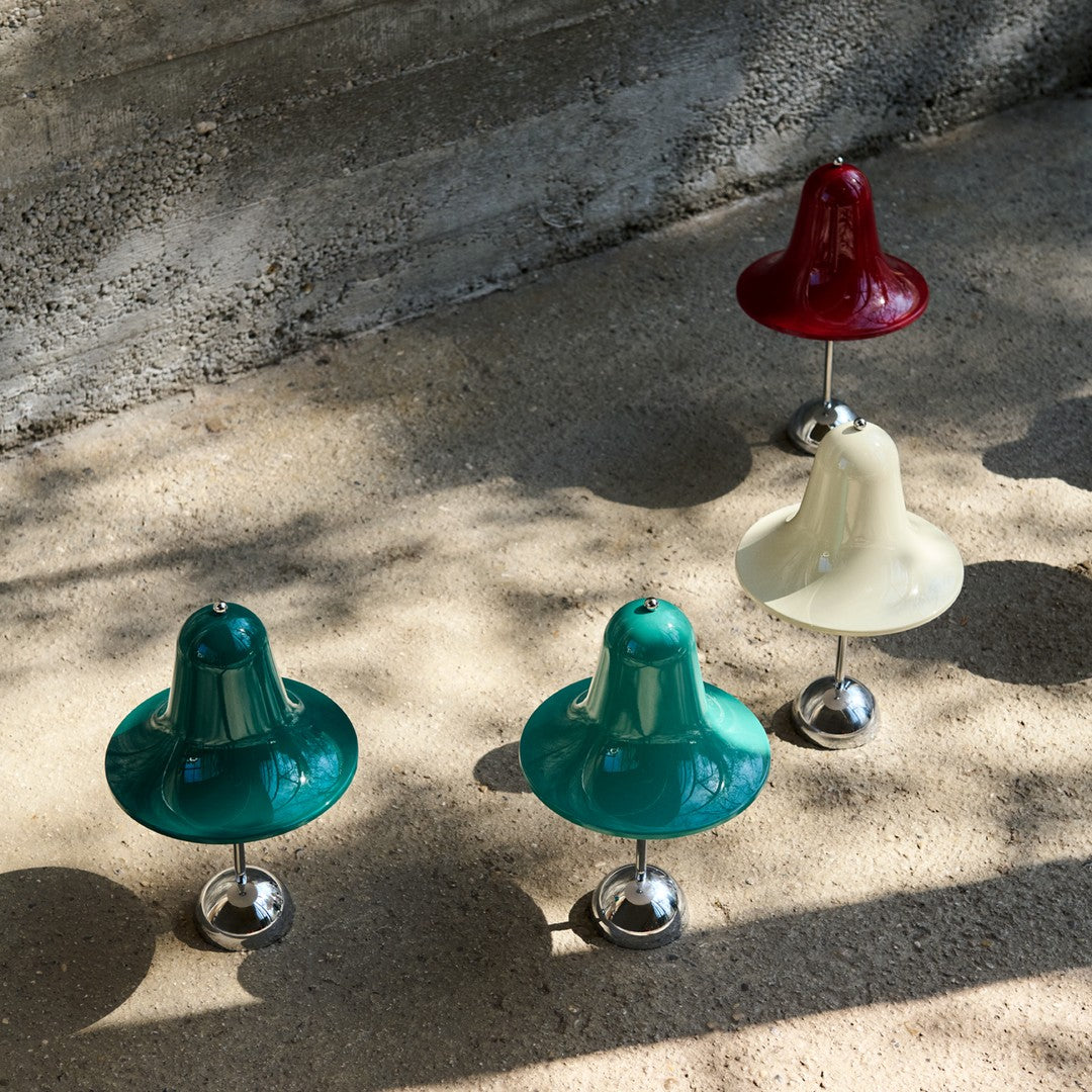 Colorful decorative bells in green, red, and white with glossy finishes and metallic bases, set on a neutral background.