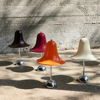Glossy bell-shaped vases in dark brown, burgundy, orange, and cream with chrome bases against a textured background.