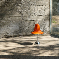 Bright orange bell-shaped chair on a sleek chrome base against a textured concrete background.