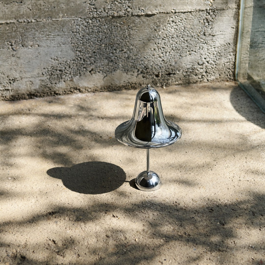 Shiny chrome bell-shaped decor on sandy surface, featuring smooth reflective surface and subtle shadows.