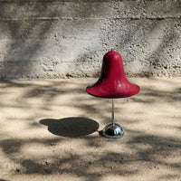 Glossy burgundy bell-shaped stool with a shiny silver base, set against a textured neutral background.