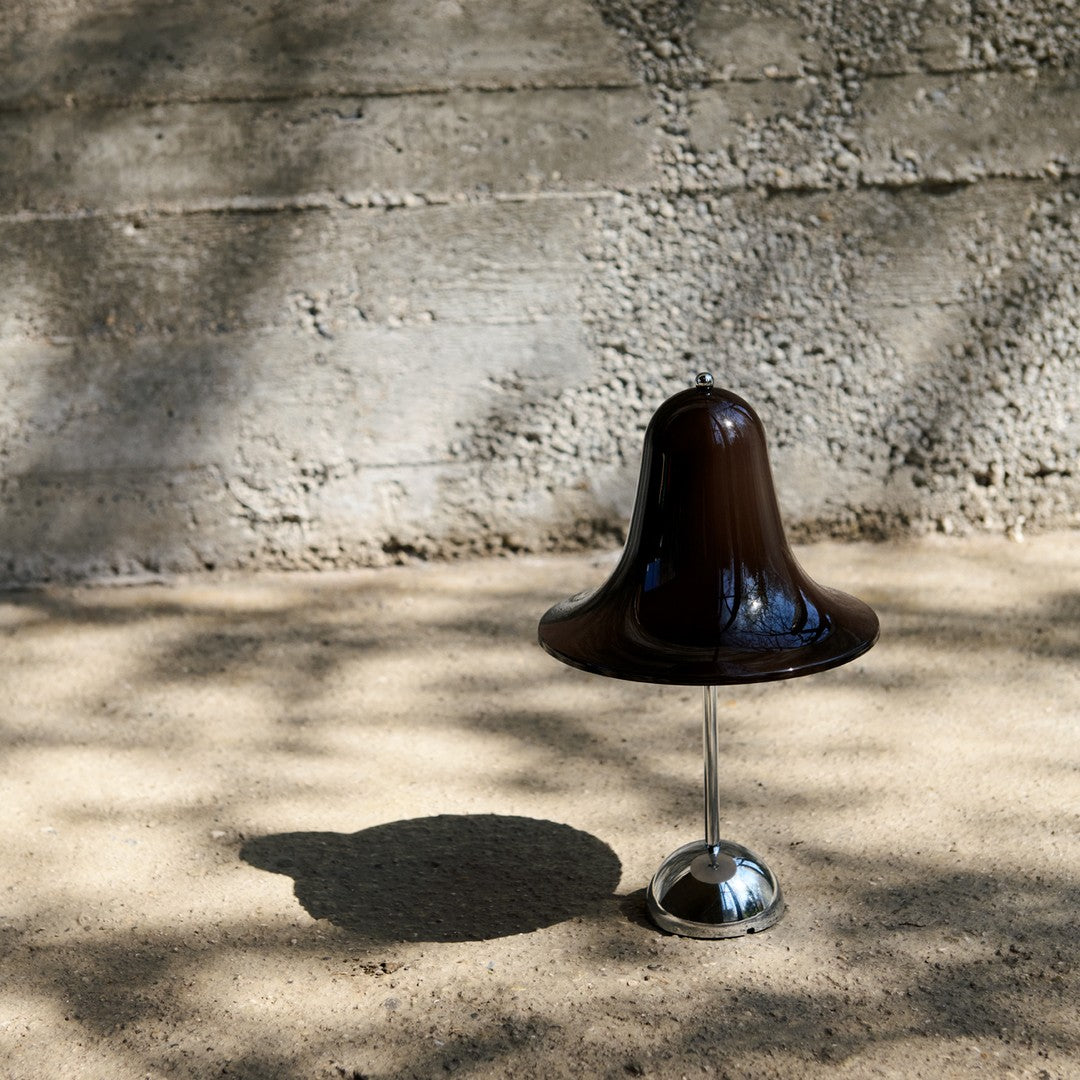 Brown bell-shaped lamp with a glossy finish on a silver base, set against a textured concrete background.