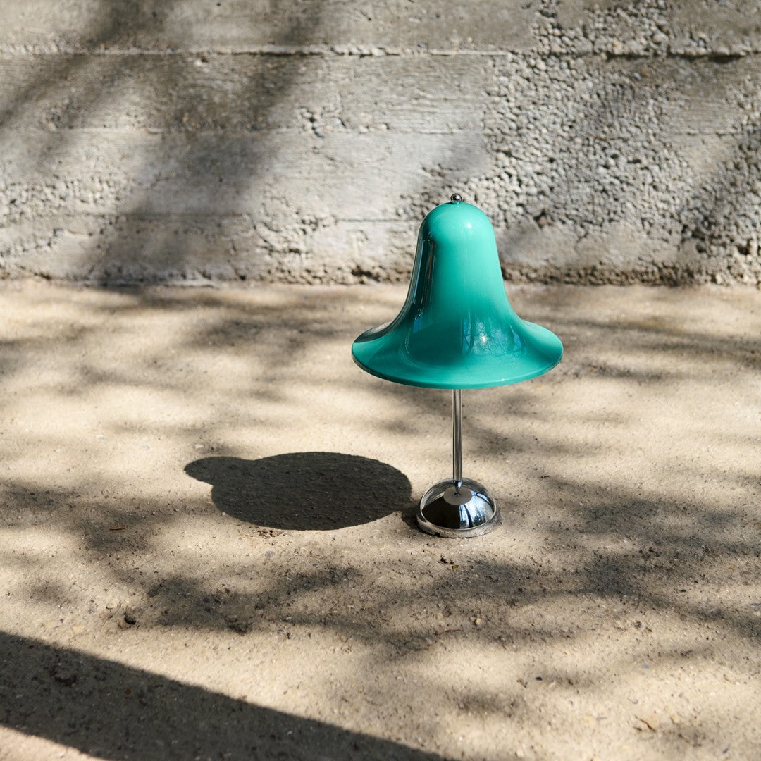 Teal bell-shaped lamp with a shiny chrome base, casting soft shadows on a textured surface.